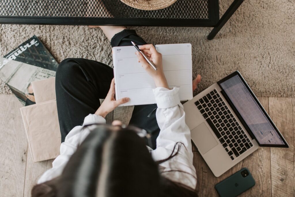 Girl Working on a laptop and also holding a book and pen